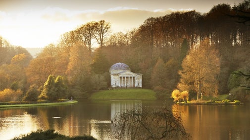 A Grecian-style building viewed from across a lake with a bridge in the left foreground, bathed in winter light